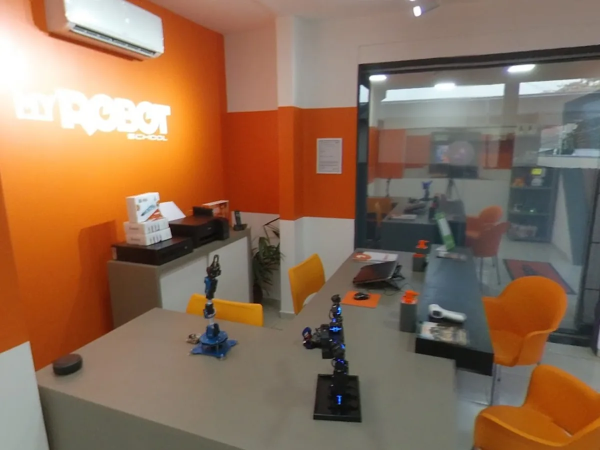 Recepção da My Robot Campo Grande: parede laranja com o logotipo iluminado, balcão com robôs expostos e poltronas de espera