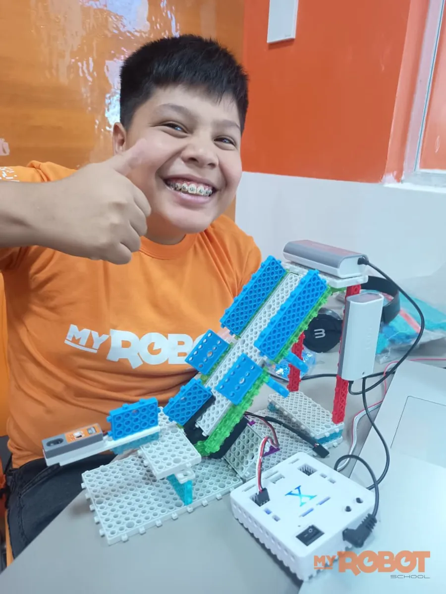Aluno da My Robot Campo Grande fazendo joinha ao lado do projeto de robótica que acabou de montar