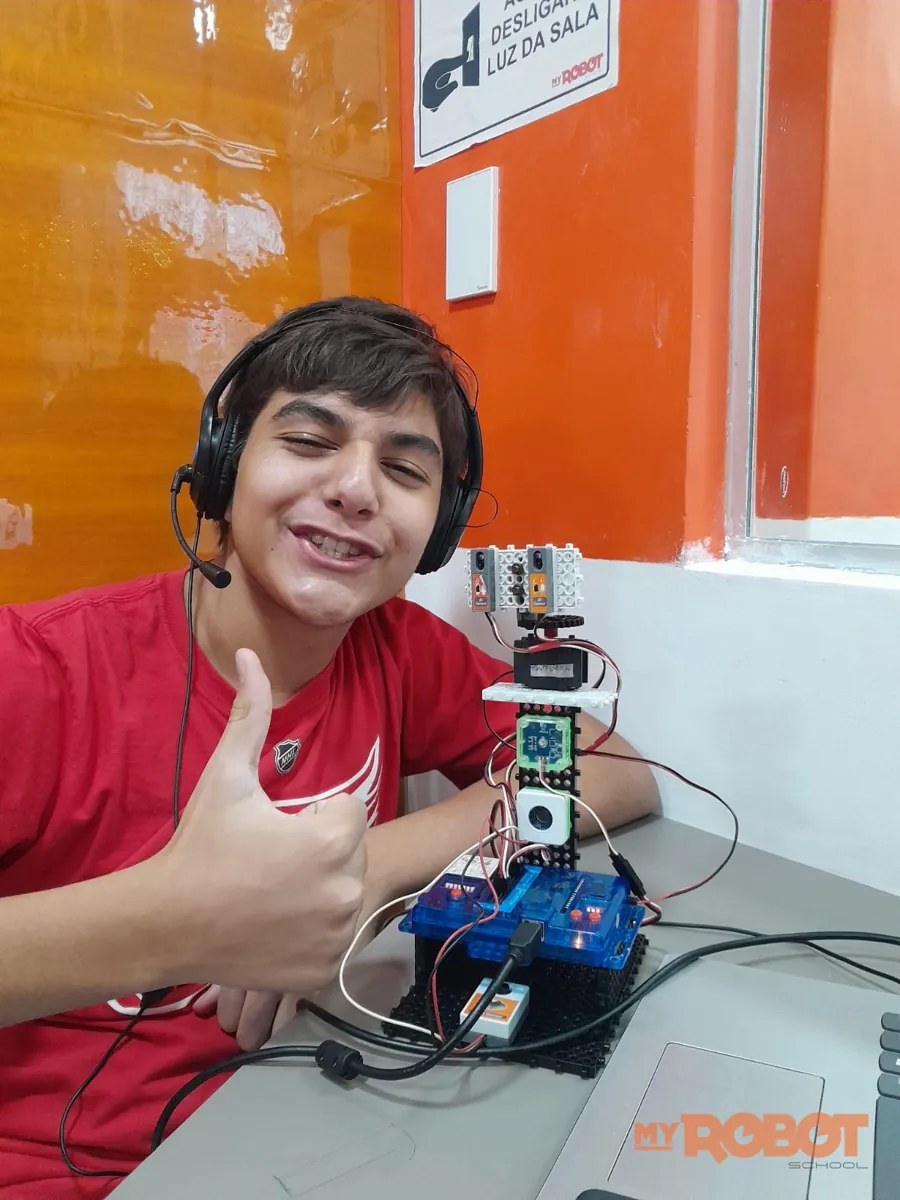 Adolescente de fone fazendo joinha ao lado do projeto Techbot com placa e sensores